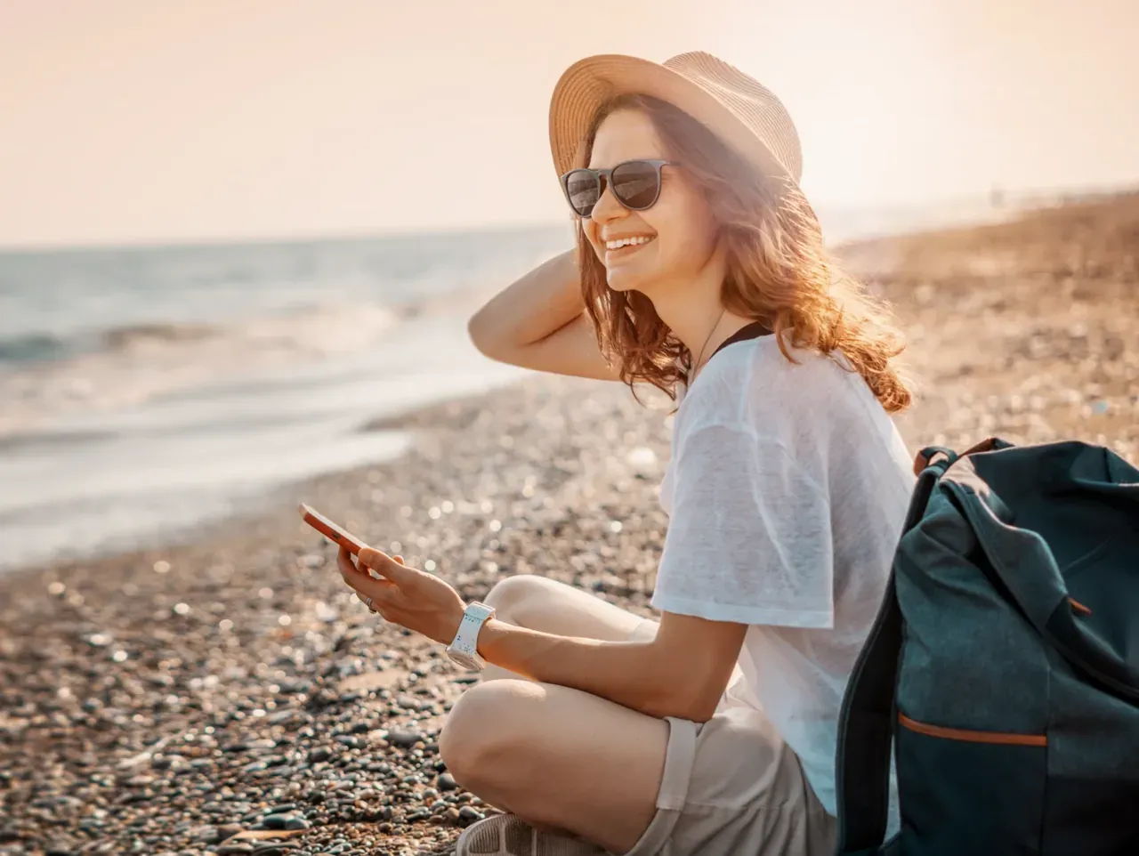 Gast sitzt mit dem Smartphone in der Hand am Strand